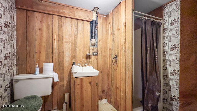 full bathroom featuring toilet, a sink, a shower with shower curtain, and wooden walls