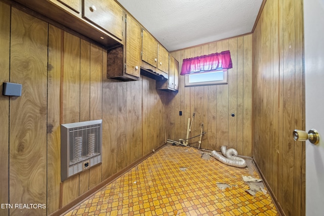 clothes washing area featuring light floors, wooden walls, cabinet space, and heating unit
