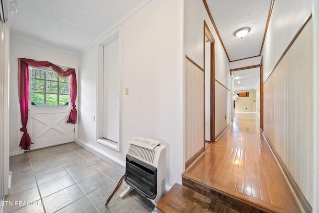 hall with a textured ceiling, crown molding, baseboards, and heating unit