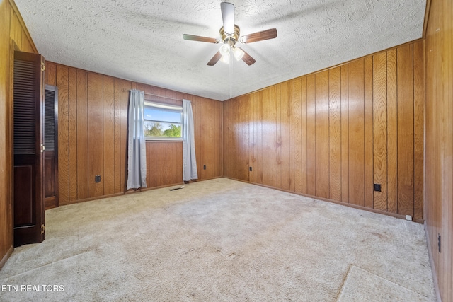 carpeted spare room featuring wood walls, visible vents, a textured ceiling, and ceiling fan