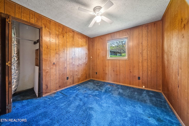 unfurnished bedroom featuring wooden walls, ceiling fan, a textured ceiling, and carpet floors