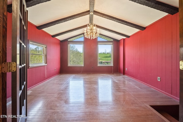 empty room with wooden walls, wood-type flooring, vaulted ceiling with beams, and a chandelier