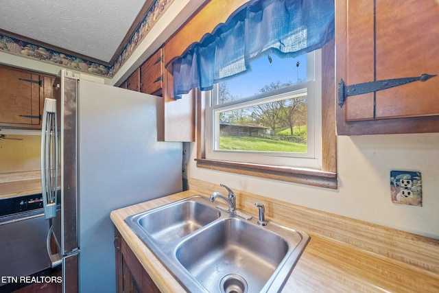 kitchen featuring a sink, light countertops, freestanding refrigerator, a textured ceiling, and brown cabinets
