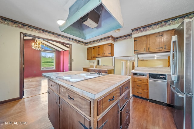 kitchen featuring light countertops, light wood-type flooring, freestanding refrigerator, under cabinet range hood, and white electric cooktop