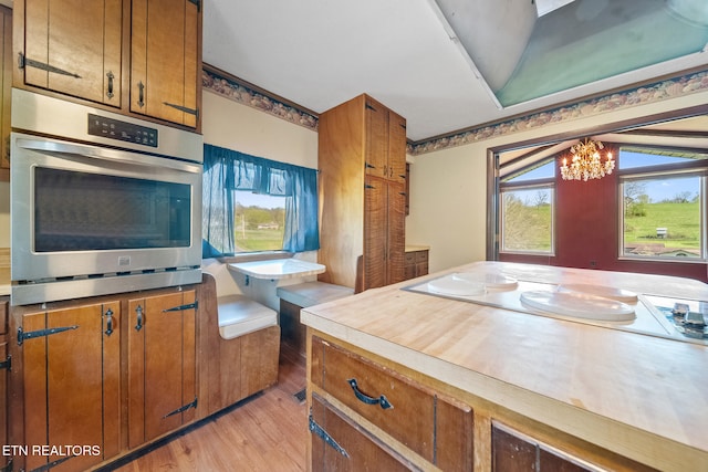 kitchen with light wood-style flooring, a chandelier, stainless steel oven, and brown cabinetry
