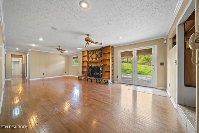 unfurnished living room with crown molding, a stone fireplace, a ceiling fan, and plenty of natural light