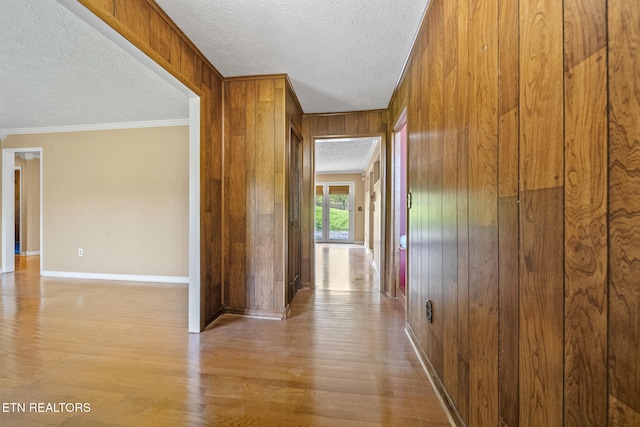 hall with baseboards, ornamental molding, a textured ceiling, wood finished floors, and wood walls