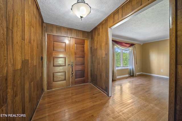 entrance foyer featuring crown molding, wood walls, wood finished floors, and a textured ceiling