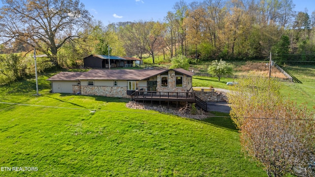 back of house with stone siding, a lawn, fence, an outdoor structure, and an outbuilding