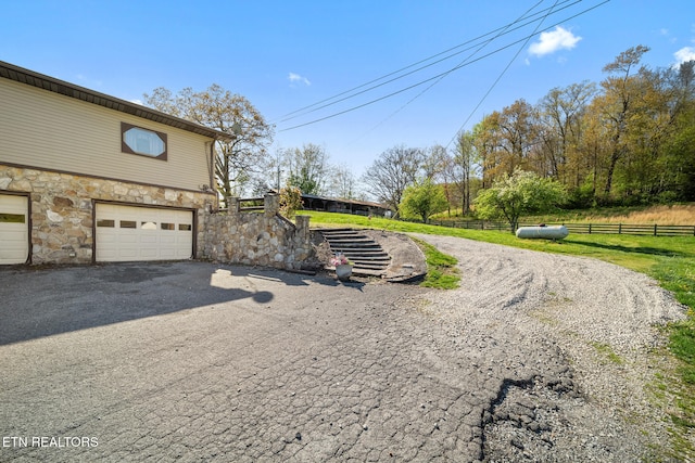 view of side of property featuring driveway, stone siding, fence, and an attached garage