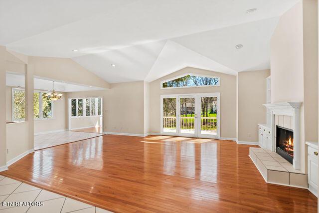unfurnished living room featuring lofted ceiling, a tile fireplace, light wood-type flooring, baseboards, and a notable chandelier