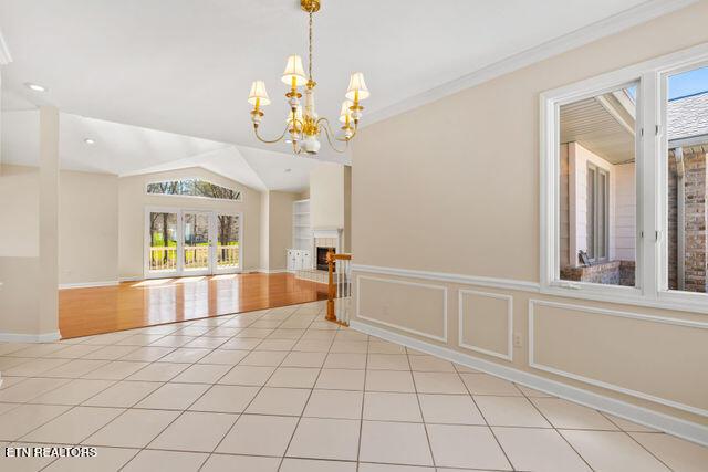 empty room featuring vaulted ceiling, crown molding, light tile patterned floors, baseboards, and a notable chandelier