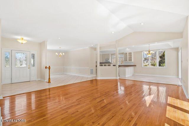 foyer entrance featuring vaulted ceiling, baseboards, visible vents, a notable chandelier, and light wood-style floors