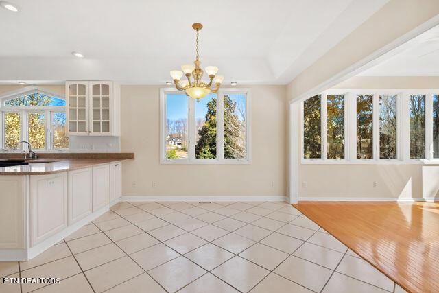 unfurnished dining area with baseboards, light tile patterned flooring, a chandelier, and a healthy amount of sunlight