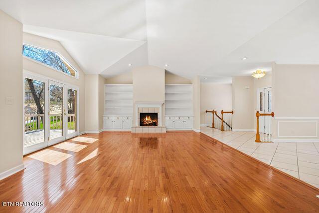unfurnished living room featuring light wood-style floors, vaulted ceiling, a tile fireplace, and baseboards