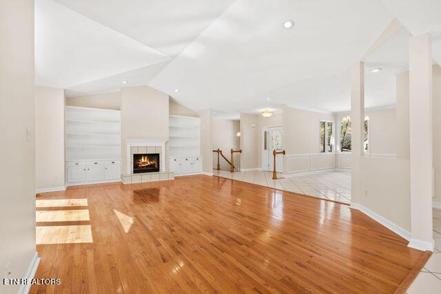 unfurnished living room with light wood-type flooring, a tiled fireplace, lofted ceiling, and built in shelves