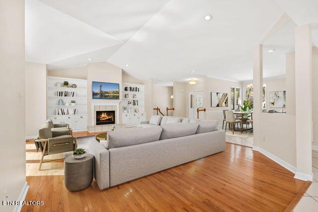 living area featuring vaulted ceiling, light wood-type flooring, built in features, and baseboards