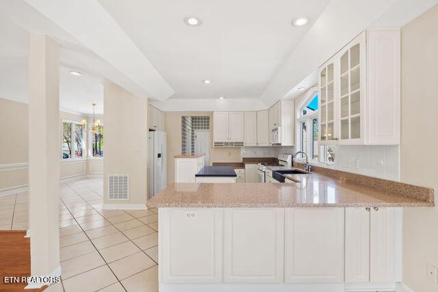 kitchen with light stone counters, visible vents, a sink, white appliances, and a peninsula