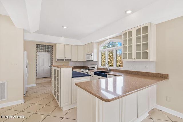 kitchen with a center island, a sink, glass insert cabinets, white appliances, and light tile patterned floors