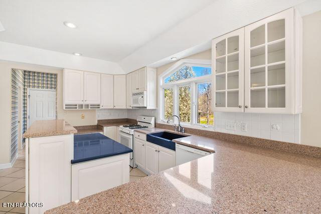 kitchen with a center island, a sink, glass insert cabinets, white appliances, and light stone countertops