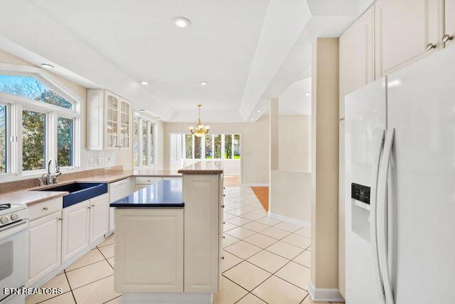 kitchen with light tile patterned floors, a sink, white appliances, a peninsula, and a notable chandelier