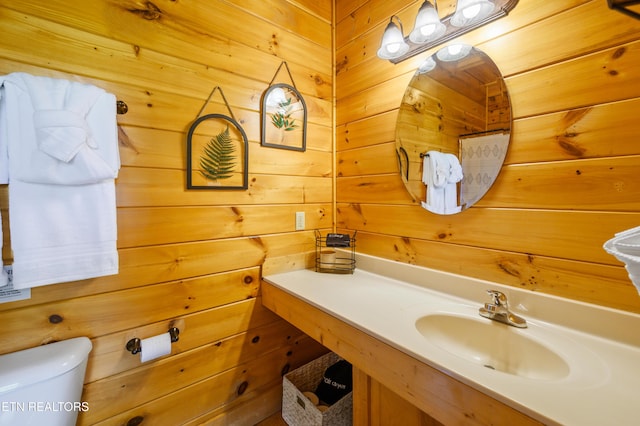 half bath with toilet, vanity, and wooden walls
