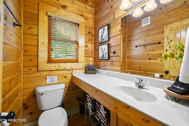 half bathroom with toilet, visible vents, vanity, and wooden walls