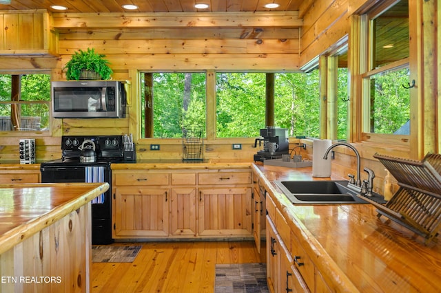 kitchen featuring stainless steel microwave, wooden counters, a sink, and black range with electric cooktop