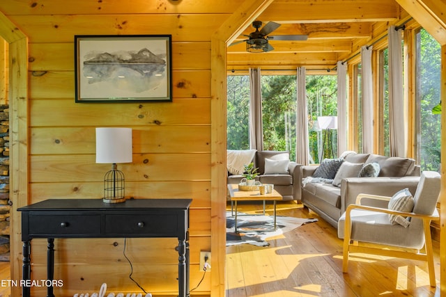 living area featuring hardwood / wood-style flooring, a wealth of natural light, a ceiling fan, and wooden walls