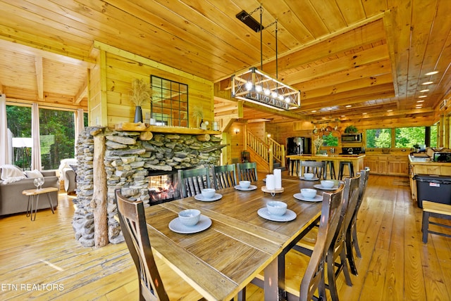 dining space featuring stairway, wood walls, wood ceiling, a fireplace, and light wood-style flooring