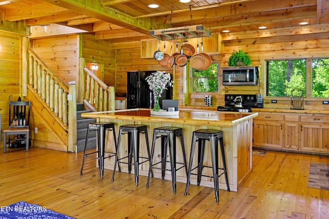 kitchen with stainless steel microwave, light wood-style floors, a center island, wood ceiling, and black electric range