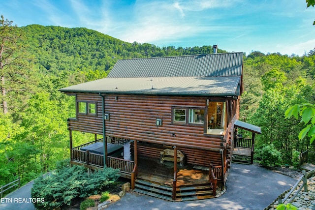 back of property featuring a deck, a view of trees, and metal roof