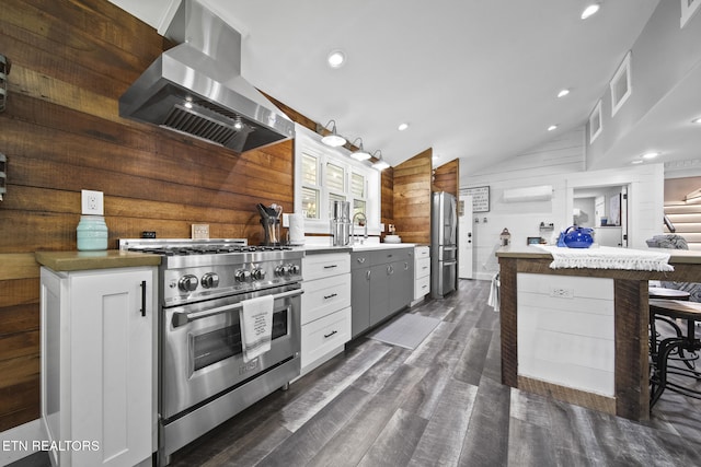 kitchen featuring an AC wall unit, lofted ceiling, appliances with stainless steel finishes, wood walls, and range hood