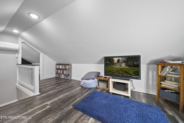 living area featuring vaulted ceiling, wood finished floors, baseboards, and a wall mounted air conditioner