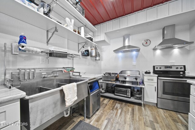 kitchen featuring stainless steel electric stove, light wood-style floors, wall chimney exhaust hood, and open shelves