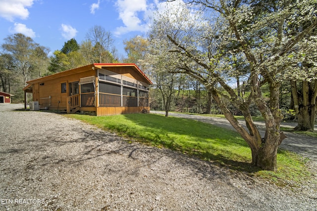 view of front of property with central air condition unit, a sunroom, a front yard, and driveway