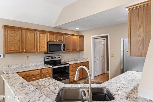 kitchen featuring lofted ceiling, light stone counters, stainless steel appliances, a sink, and brown cabinetry