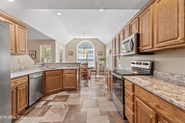 kitchen featuring a sink, a textured ceiling, appliances with stainless steel finishes, a peninsula, and lofted ceiling