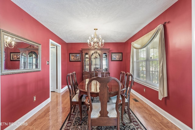 dining area with baseboards, visible vents, a chandelier, and light wood finished floors