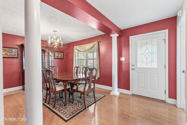 dining room with light wood-type flooring, baseboards, an inviting chandelier, and ornate columns