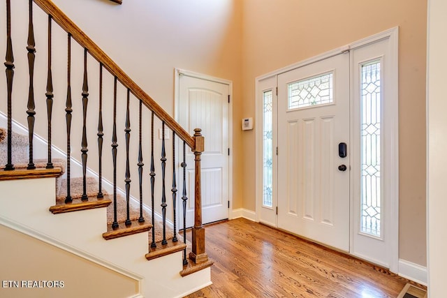 entryway featuring stairway, a high ceiling, baseboards, and wood finished floors