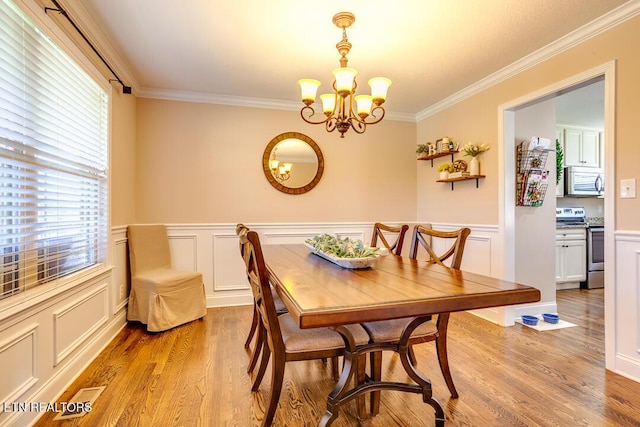 dining area with a decorative wall, ornamental molding, a chandelier, and light wood-type flooring