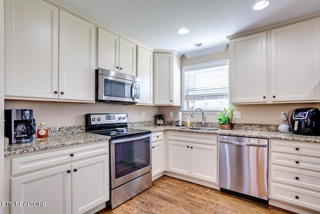 kitchen with light stone counters, a sink, light wood-type flooring, appliances with stainless steel finishes, and recessed lighting