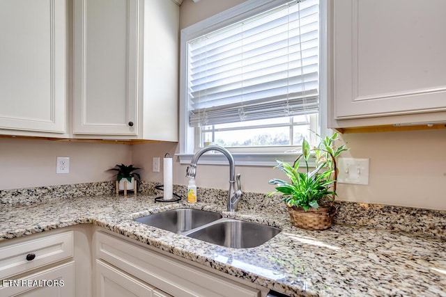 kitchen with white cabinets, light stone countertops, and a sink
