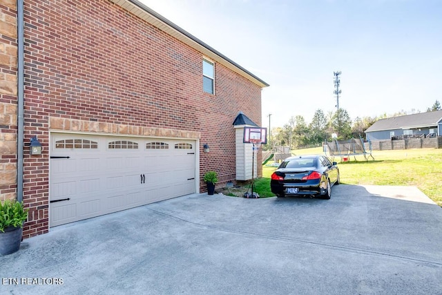 view of side of property with a lawn, concrete driveway, brick siding, and a trampoline