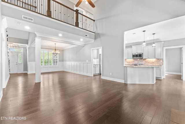 1416 Ebenezer Rd, Knoxville, TN 37922 - unfurnished living room with visible vents, crown molding, dark wood-style flooring, decorative columns, and ceiling fan with notable chandelier