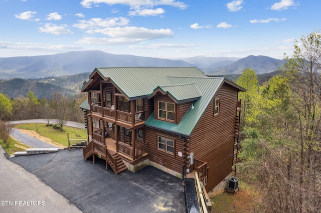 exterior space with log exterior, a mountain view, cooling unit, a balcony, and metal roof