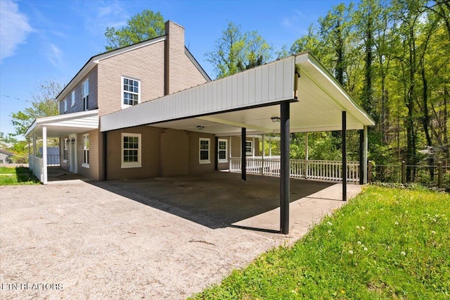 back of house with an attached carport, driveway, a chimney, fence, and brick siding