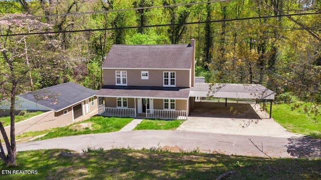 view of front of house with aphalt driveway, a front lawn, covered porch, a carport, and a view of trees