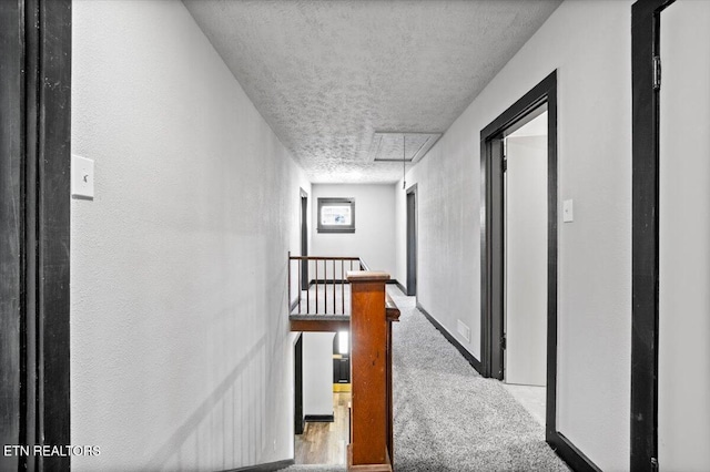 hallway featuring attic access, carpet, a textured ceiling, and an upstairs landing